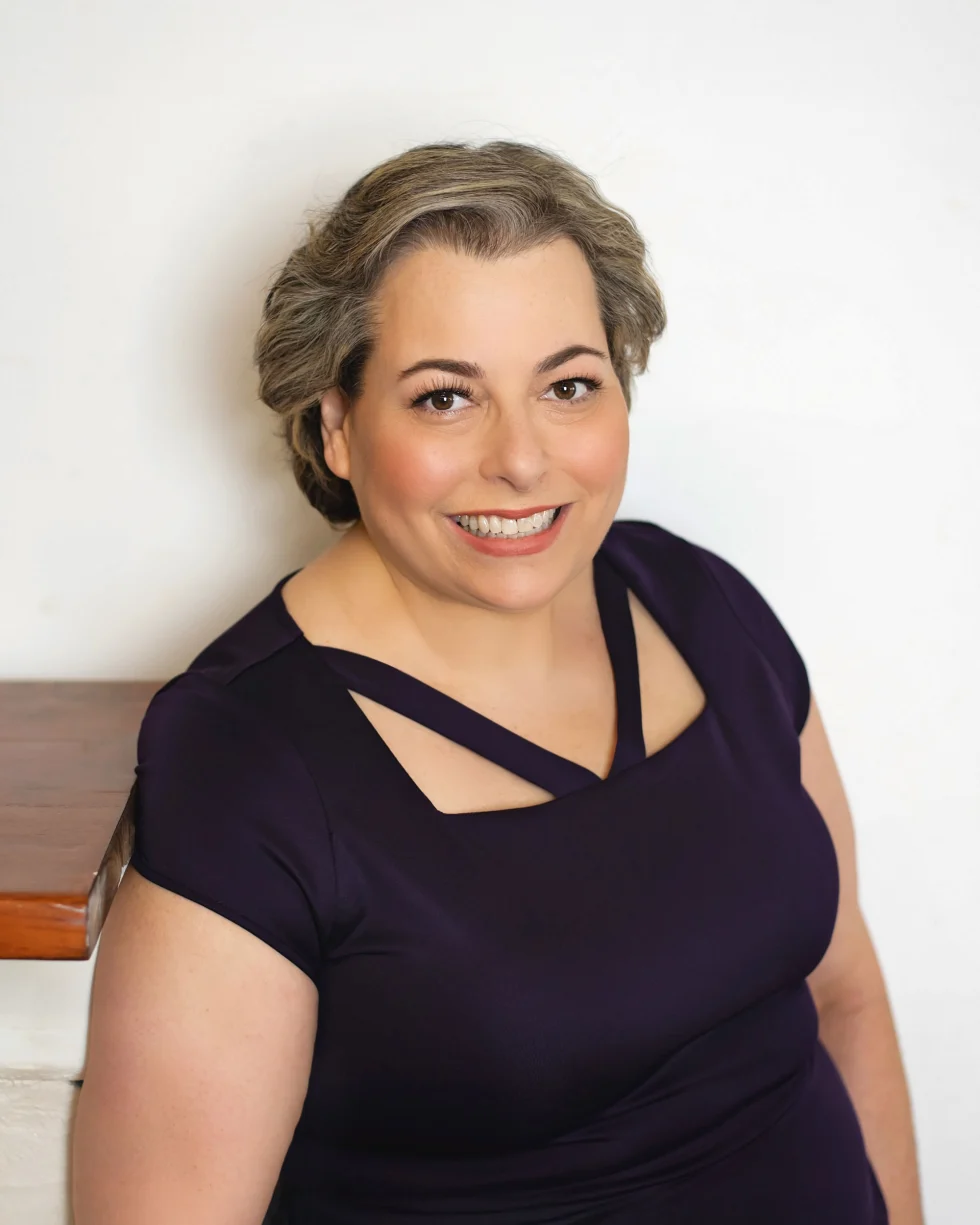 Judy, the owner of Clutter Relief Services in Hamilton Ontario, smiling at the camera. She is wearing a dark coloured shirt and is positioned against a white wall.