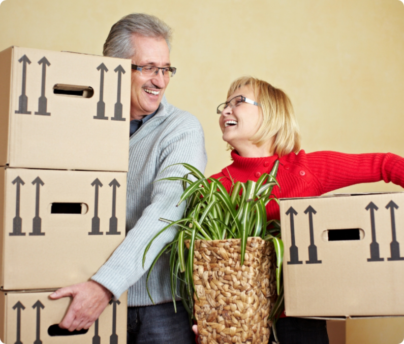 A senior couple smiling at each other, holding moving boxes